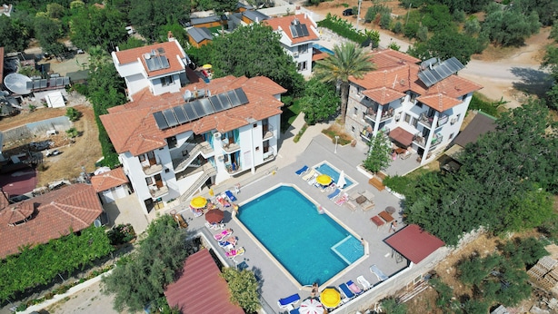 An aerial view of a residential area with a swimming pool surrounded by lounge chairs and umbrellas, solar panels on the roofs, and a red-roofed building.