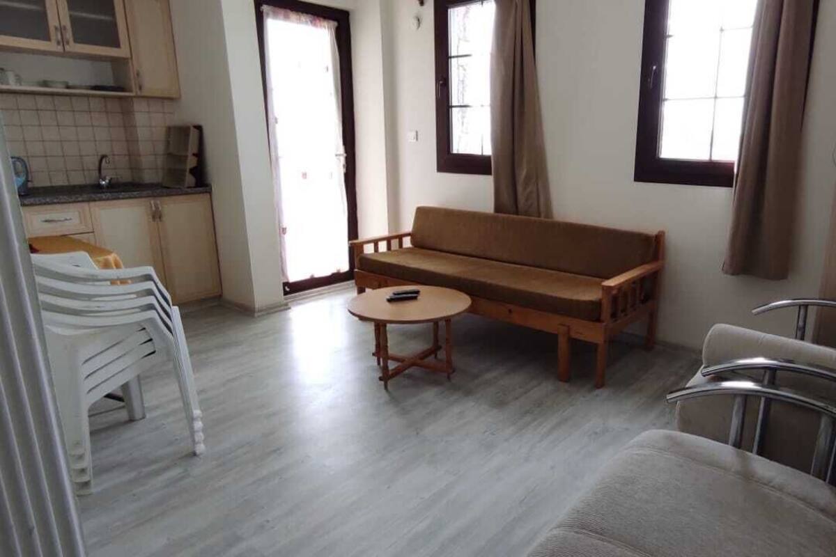 A living area with a sofa, a round table, a chair, and a kitchen area with cabinets and a window.