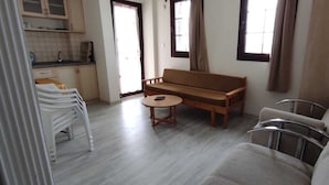A living area with a sofa, a round table, a chair, and a kitchen area with cabinets and a window.