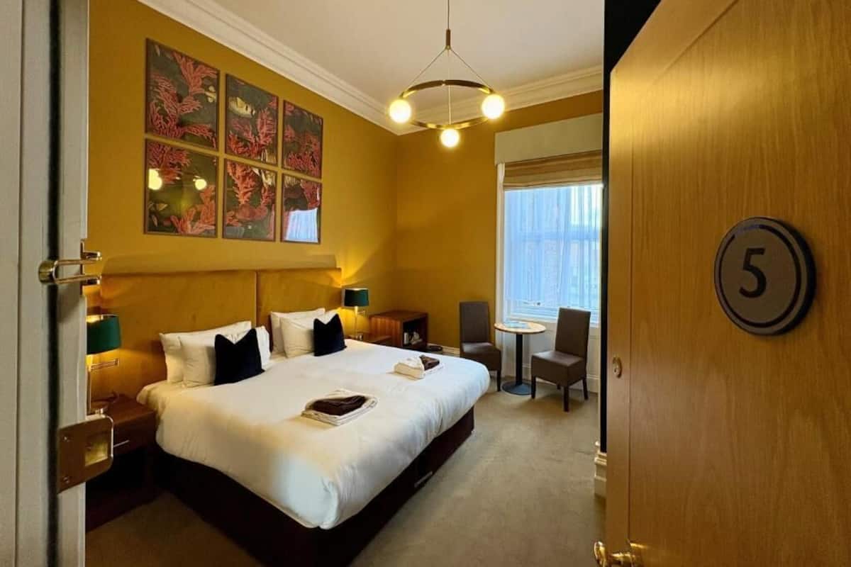 A hotel room with a large bed, a desk, a chair, a small table, and a window.