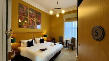 A hotel room with a large bed, a desk, a chair, a small table, and a window.