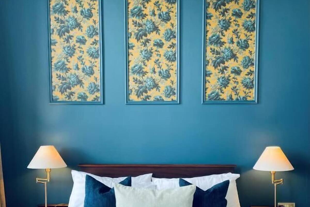 A hotel room with a bed, two bedside tables, two lamps, and three floral wall art pieces.