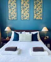A hotel room with a bed, two bedside tables, two lamps, and three floral wall art pieces.