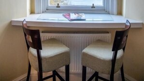 Una habitación con ventana que da al mar, un escritorio blanco, dos sillas y un radiador debajo.