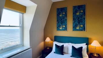 A hotel room with a bed, two bedside lamps, a window with a view, and two wall art pieces.