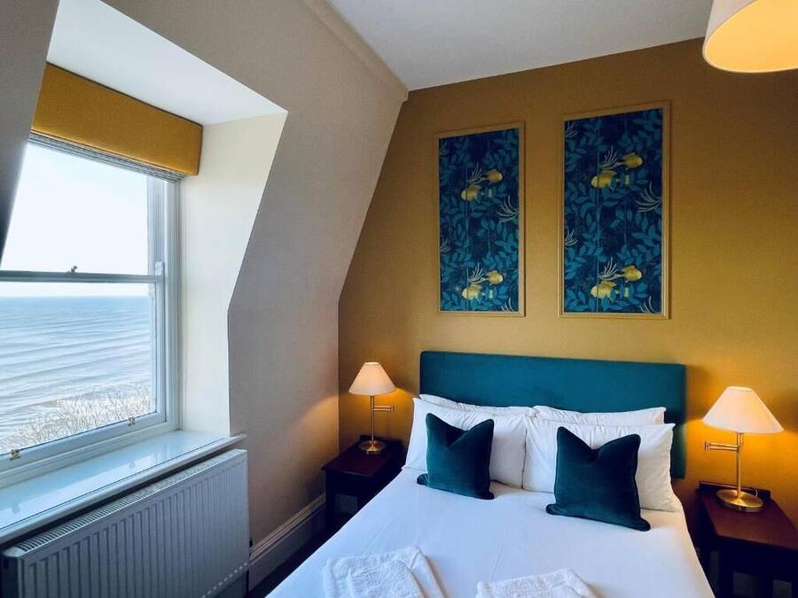 A hotel room with a bed, two bedside lamps, a window with a view, and two wall art pieces.