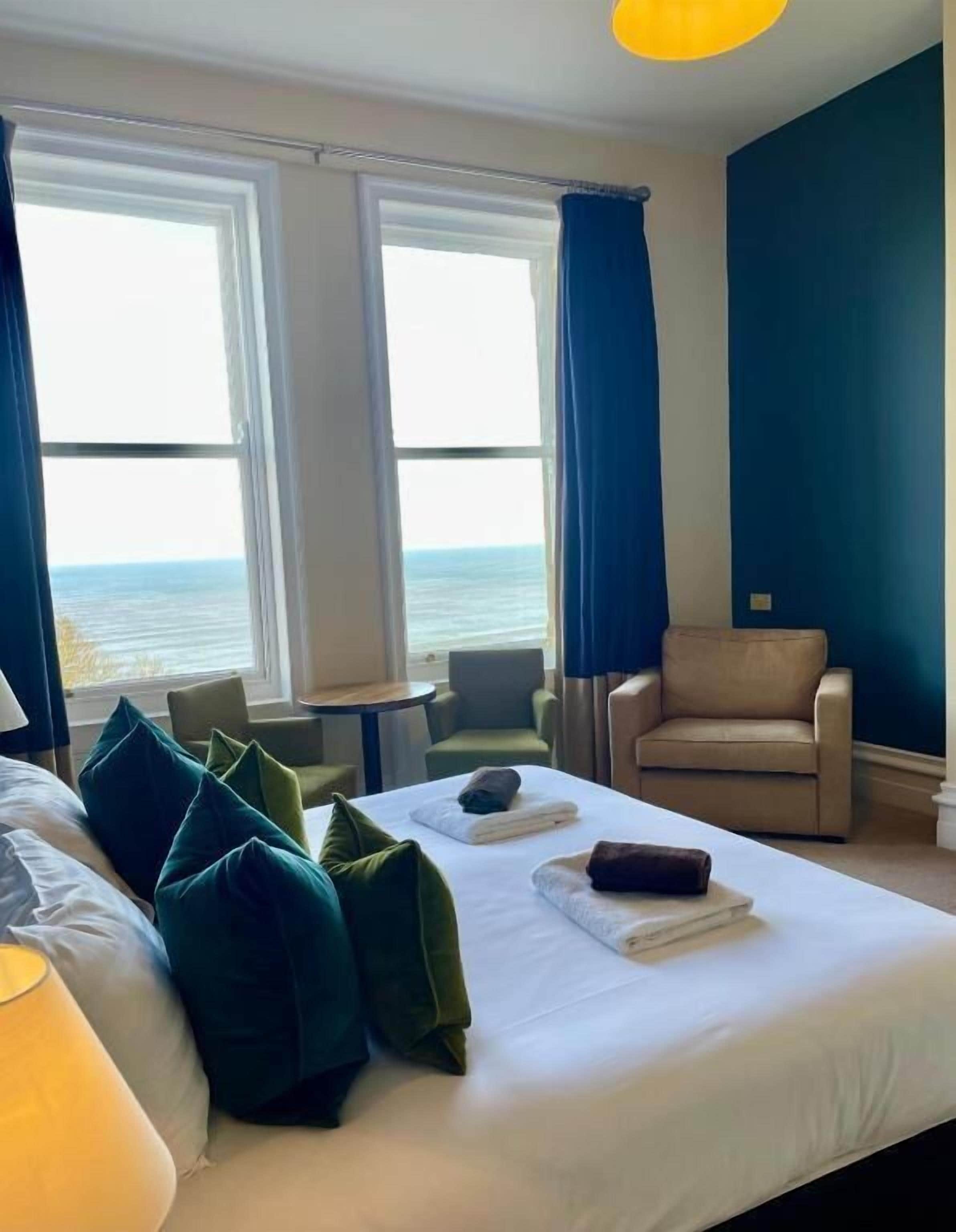 Habitación de hotel con cama, dos sillas, una mesita y vista al mar.