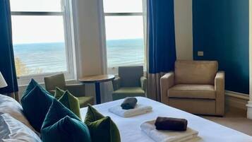 Habitación de hotel con cama, dos sillas, una mesita y vista al mar.