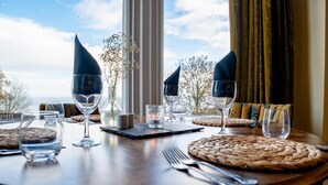 Mesa para comer dispuesta con copas de vino, cubiertos y individuales tejidos, con vista a árboles y cielo.