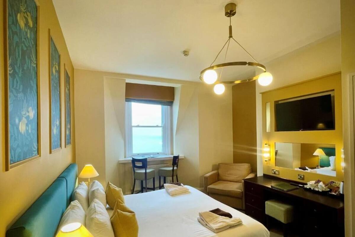 A hotel room with a bed, desk, chair, and a large mirror.