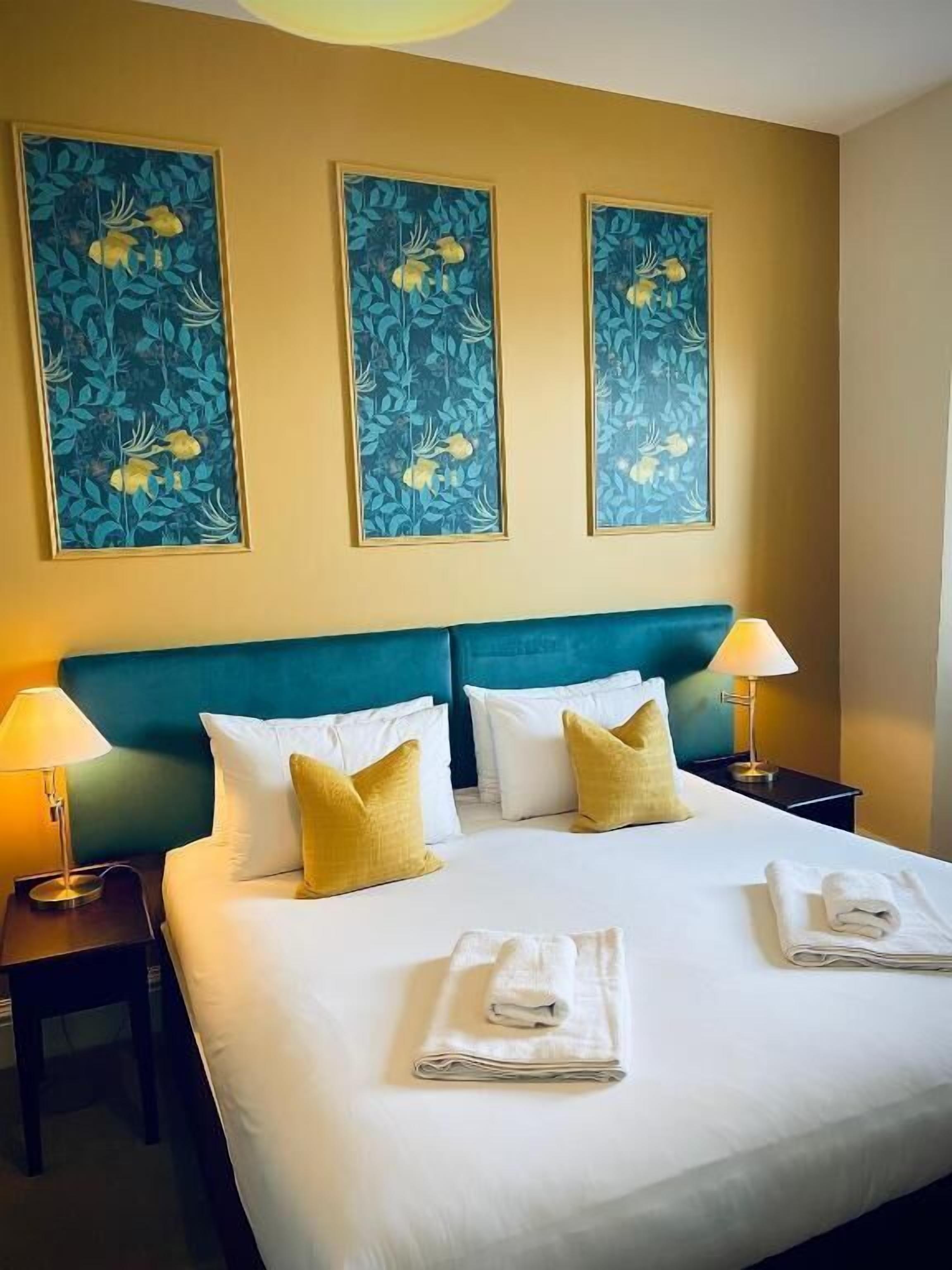 Una habitación de hotel con una cama grande, dos mesitas de noche y tres cuadros colgados en la pared.