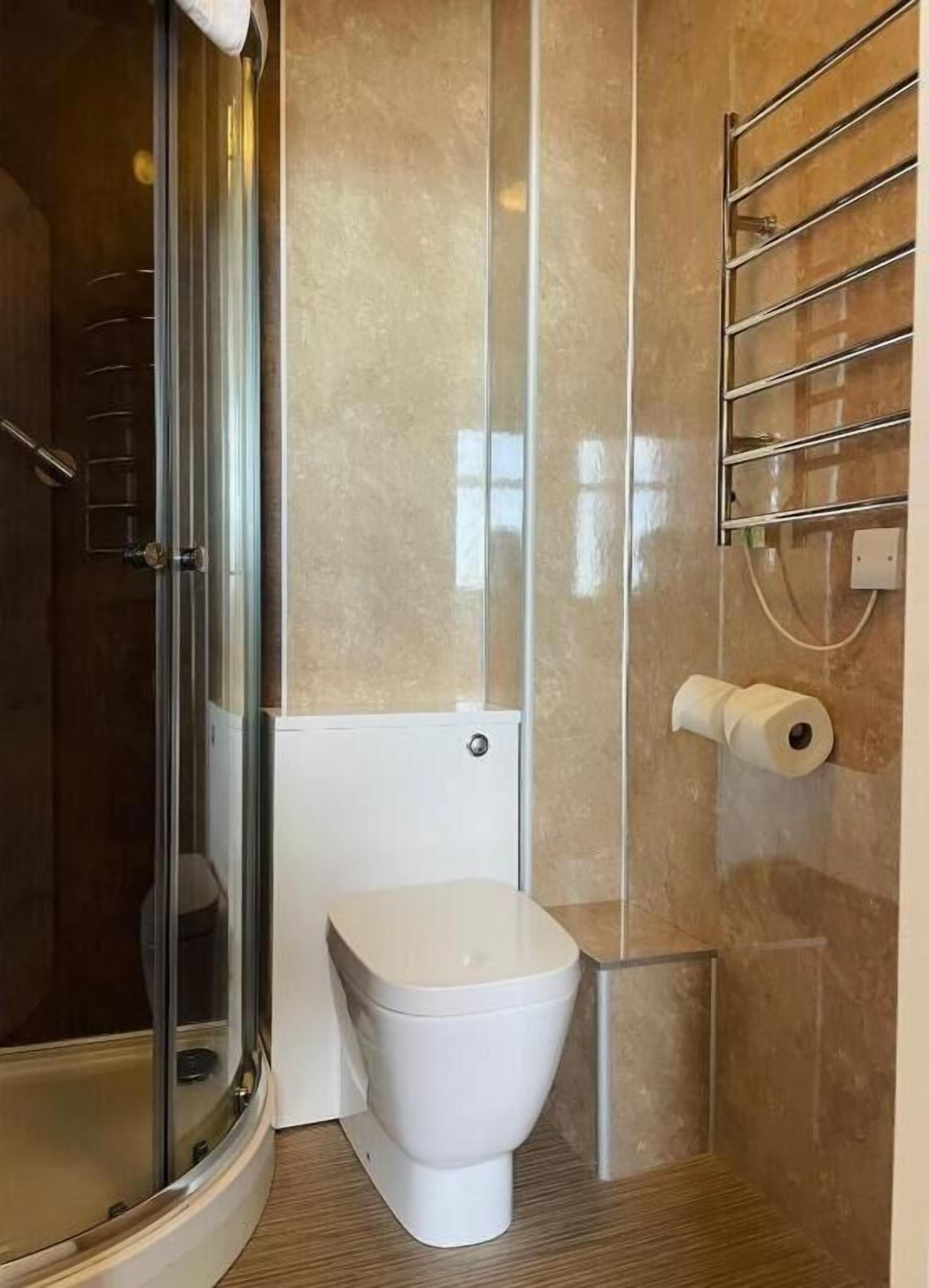 A modern bathroom with a glass shower enclosure, a toilet, and a towel rack.