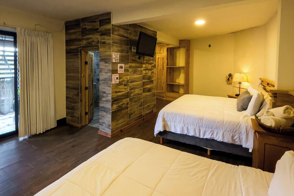 A hotel room with two beds, a television, a wooden cabinet, and a window with curtains.