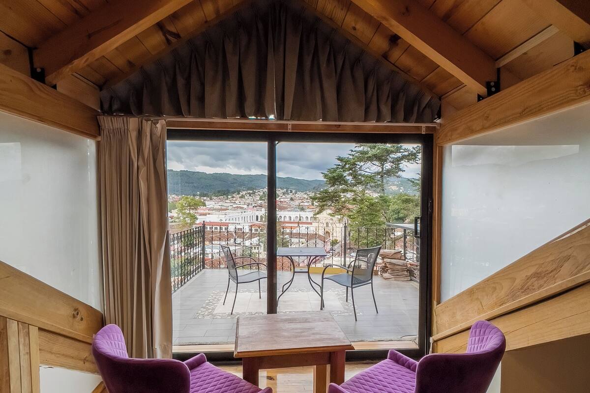 A wooden room with a large window, two purple chairs, and a table.