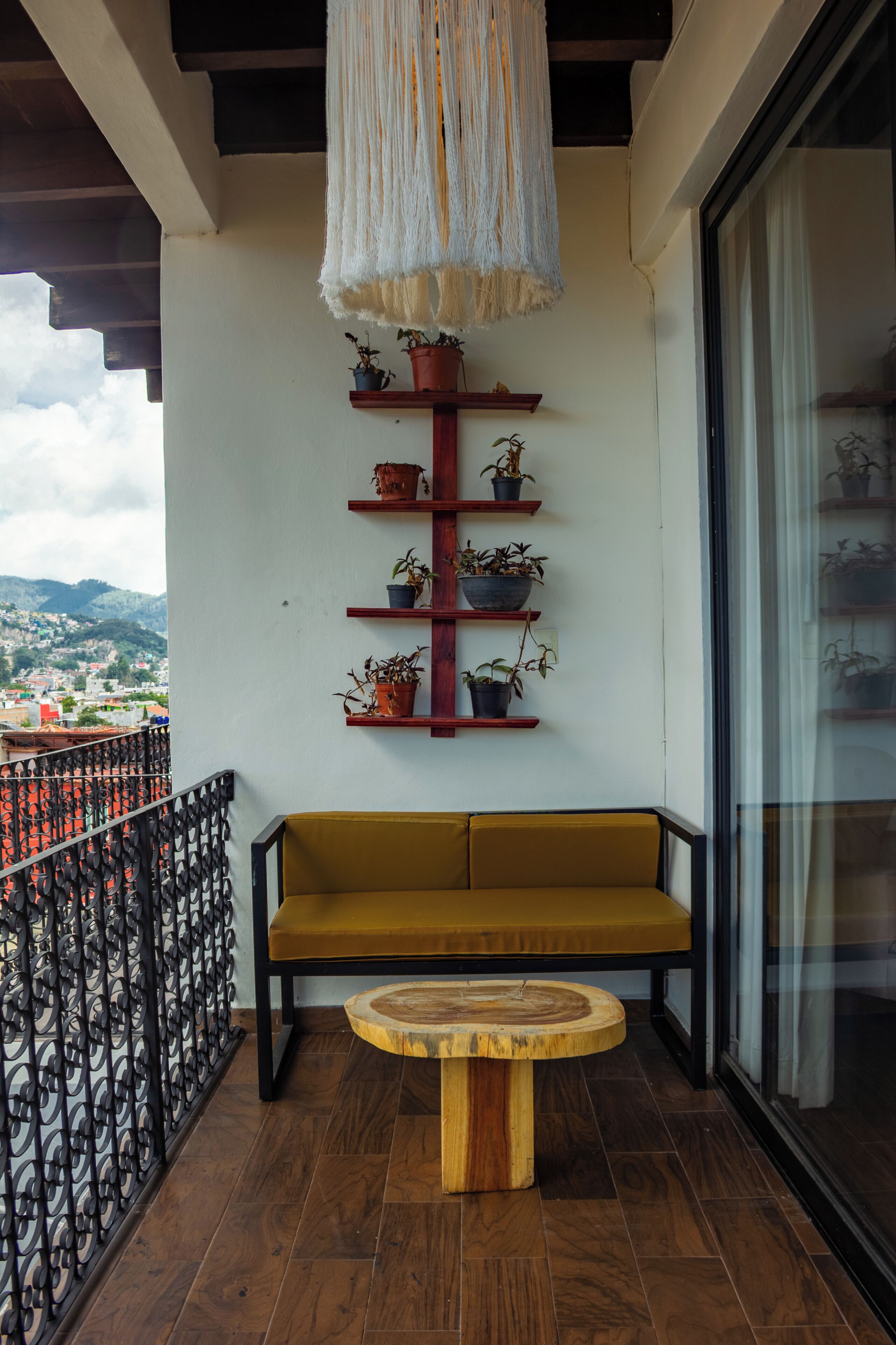 Un balcon avec un banc en bois, une table ronde et des plantes en pot disposées sur des étagères.