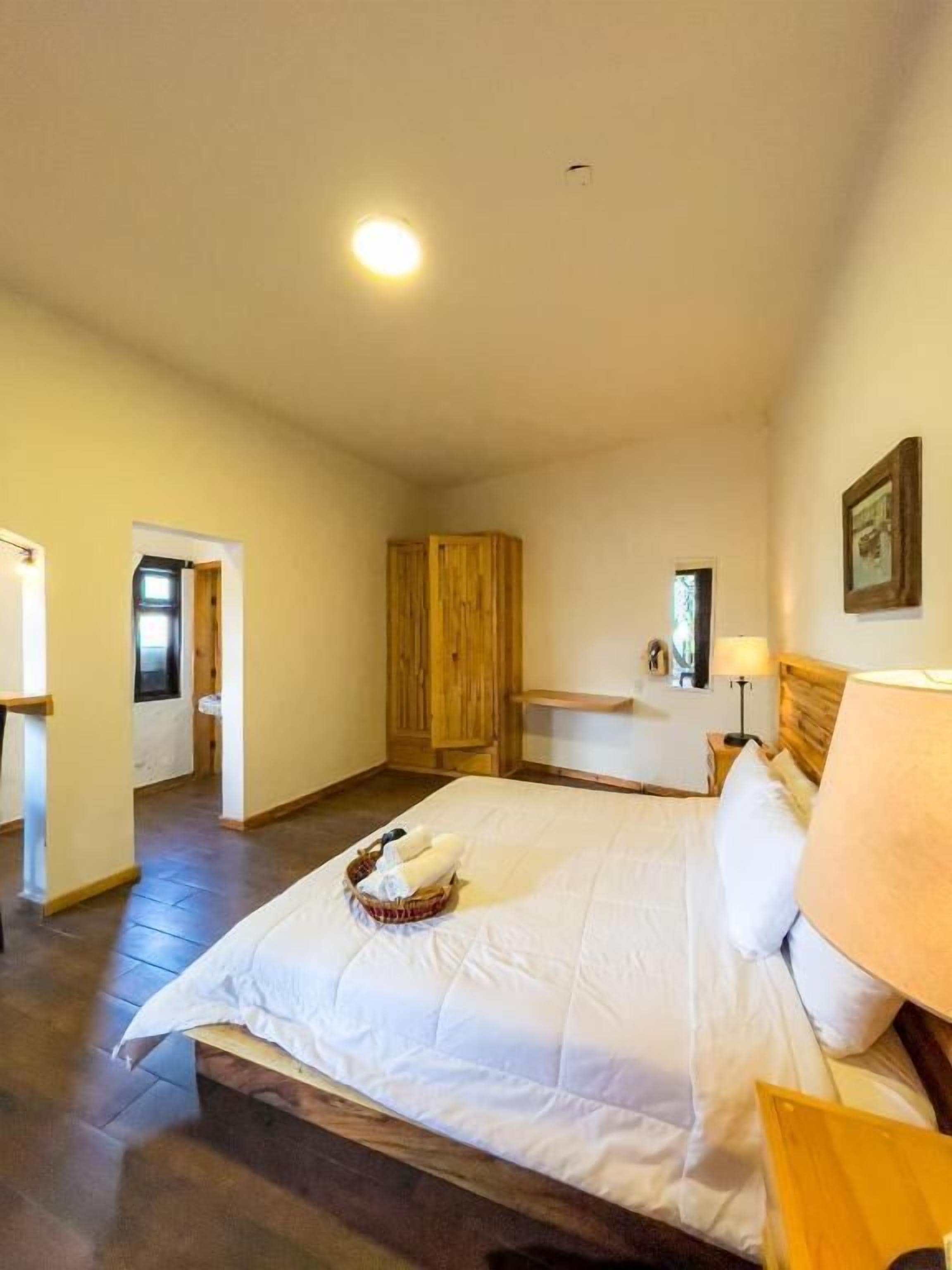 A bedroom with a bed, wooden wardrobe, bedside table, lamp, and a small bathroom.