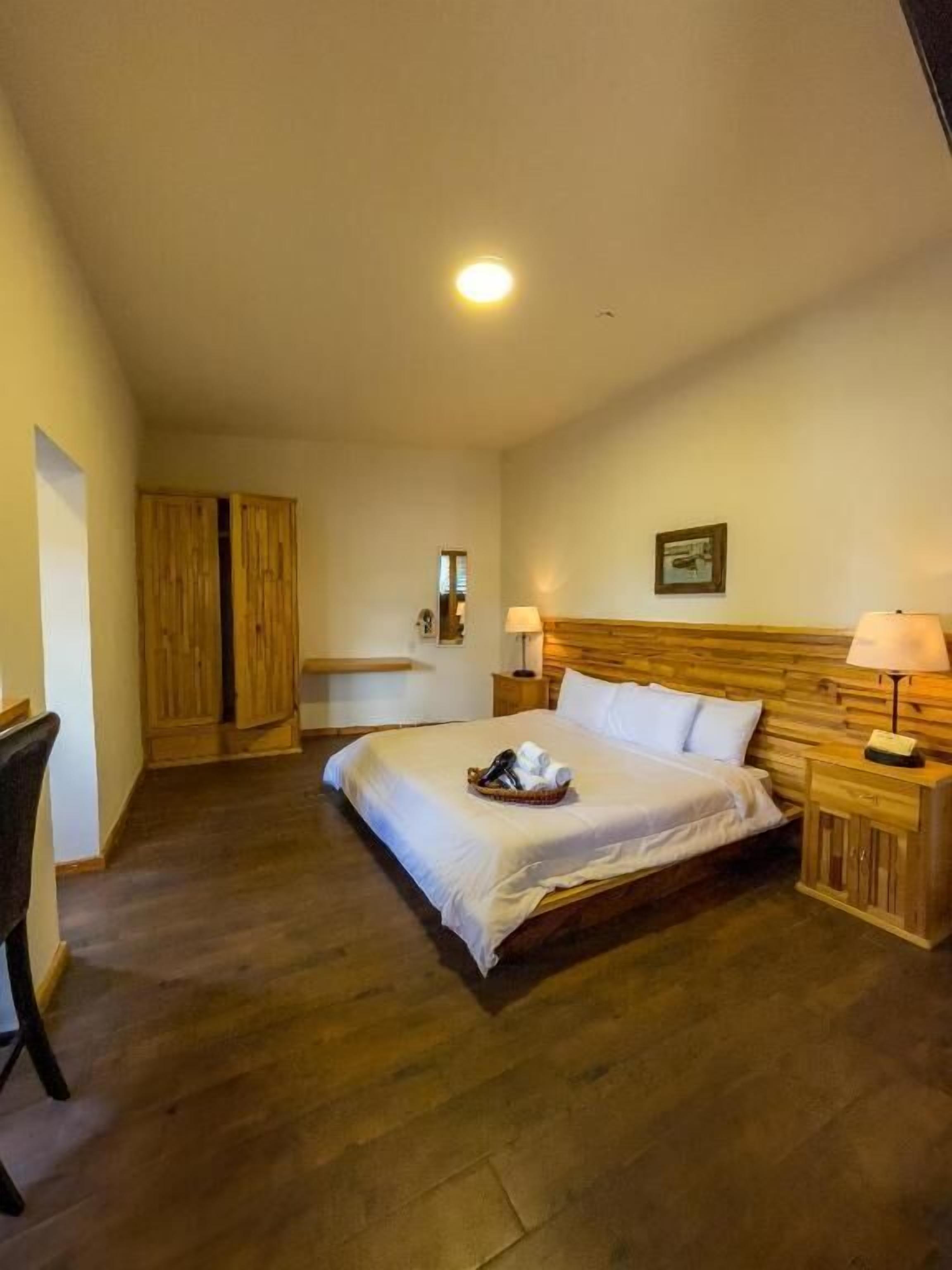 A bedroom with a wooden bed, bedside lamps, a wooden wardrobe, and a small table with a lamp.