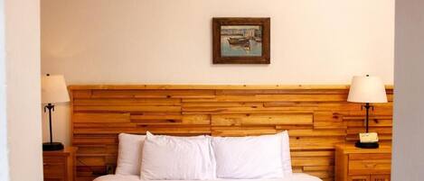 A hotel room with a wooden headboard, a bed with white bedding, two bedside lamps, and a framed picture on the wall.