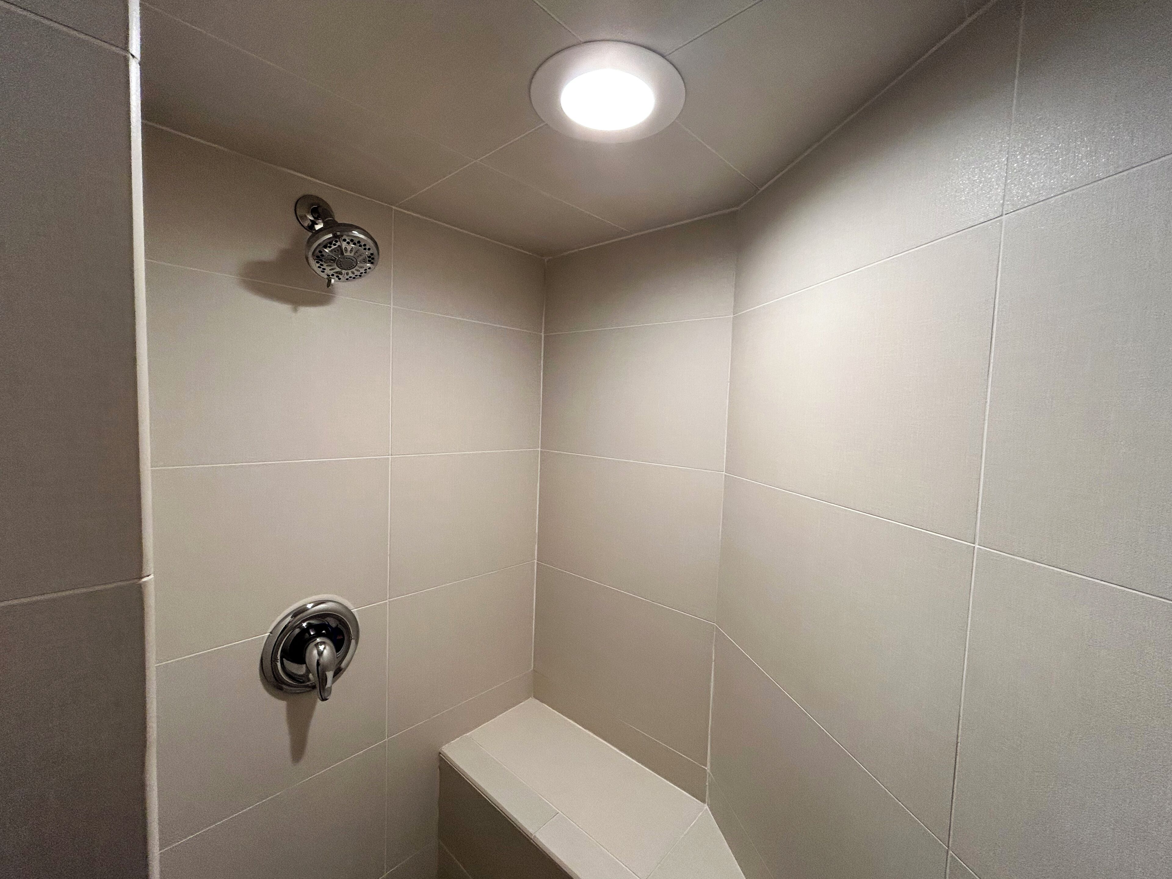 Un pequeño box de ducha con azulejos, una lámpara en el techo y un grifo de pared.