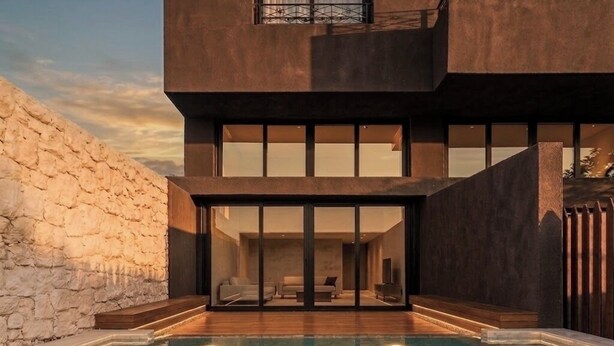 Una casa moderna con piscina, muro de piedra y amplios ventanales.
