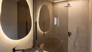 Un baño moderno con un espejo ovalado grande, un lavamanos de piedra y una ducha con mampara de vidrio.