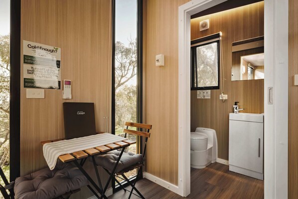Una habitación pequeña con pared de madera, una mesita con un banco, un inodoro y un lavabo.