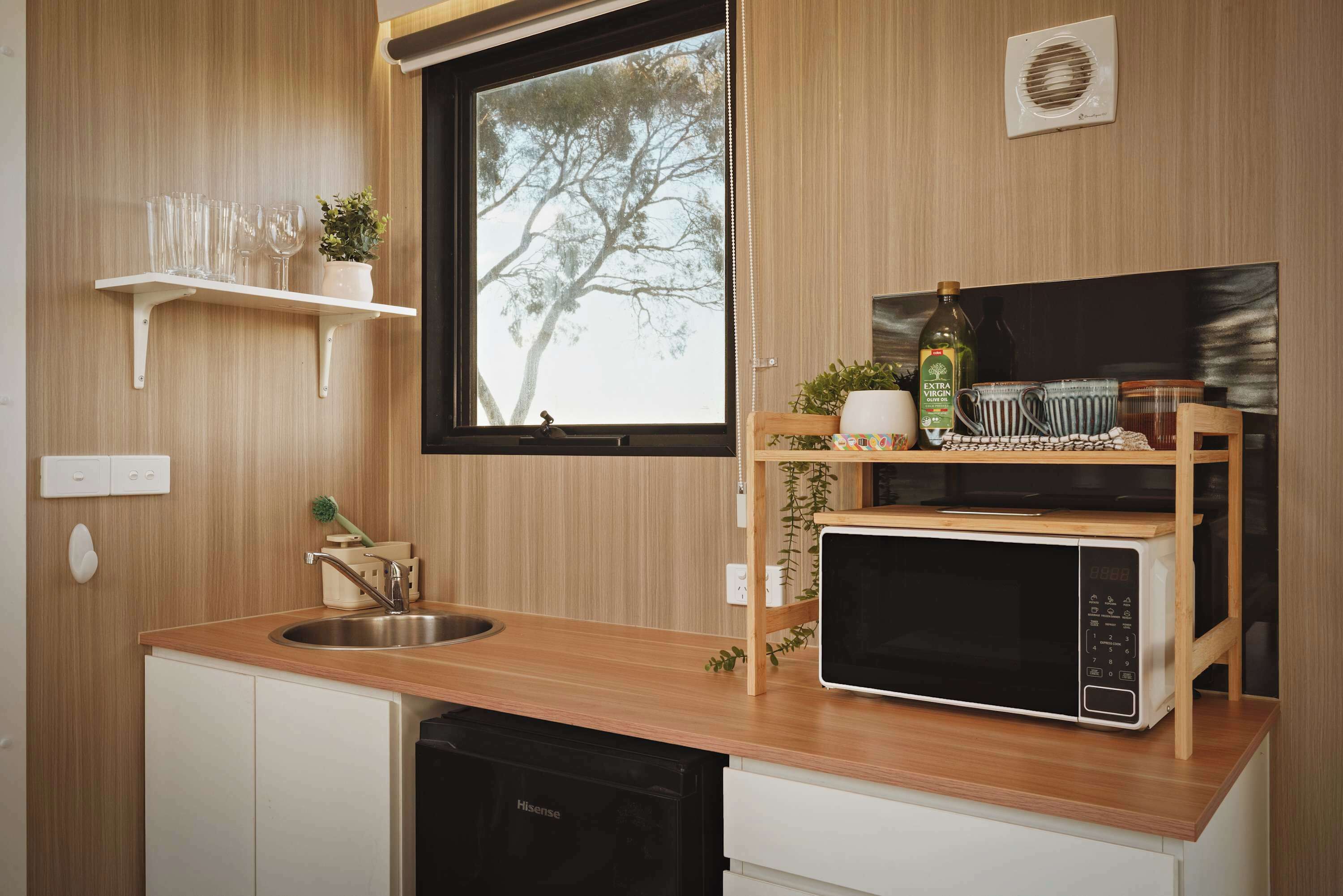 A compact kitchen with a wooden countertop, a sink, a microwave, and a window with a view of trees.