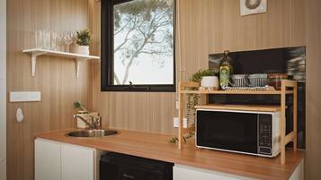 A compact kitchen with a wooden countertop, a sink, a microwave, and a window with a view of trees.