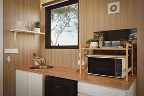 A compact kitchen with a wooden countertop, a sink, a microwave, and a window with a view of trees.