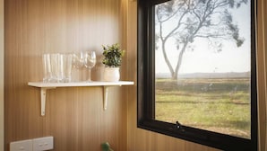 Een houten wand met een raam, een plank waarop glazen en een plant staan, en een stopcontact.