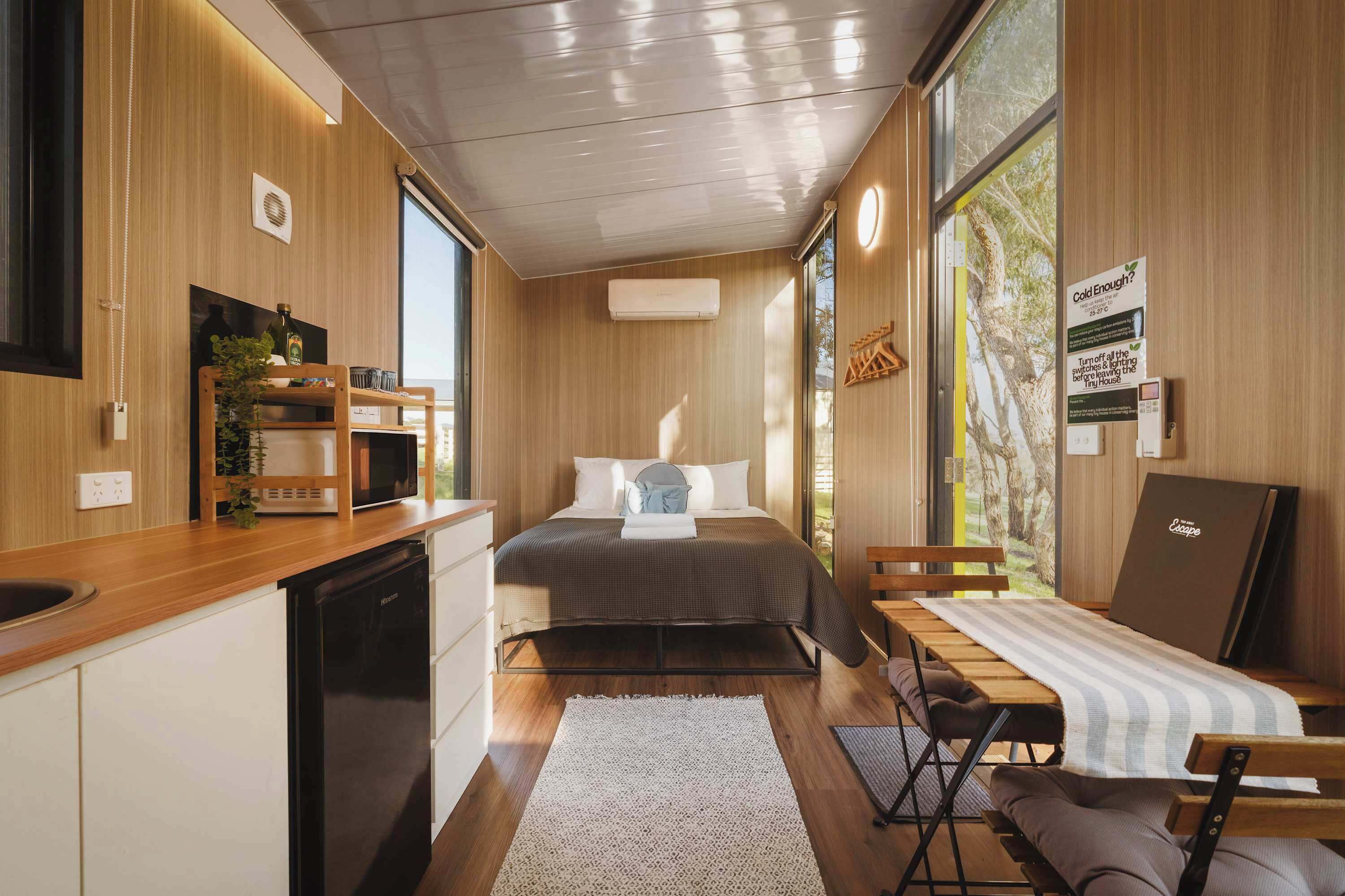 A compact room with a bed, a small desk, a chair, a sink, and a window.
