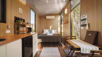 A compact room with a bed, a small desk, a chair, a sink, and a window.
