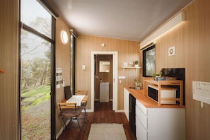 A compact kitchen with wooden walls, a dining area with a table and chairs, and a view of the outdoors.