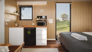 Een moderne slaapkamer met een groot bed, een houten vloer, een keuken met een magnetron en uitzicht op de omgeving.