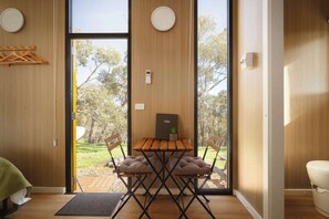 A modern interior with a wooden dining table, cushioned chairs, and a view of a garden through large windows.