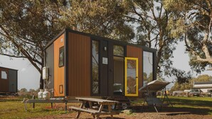 A small, modern cabin with a wooden exterior, a glass door, and a picnic table in a natural setting. - Tallarook Hilltop Tiny House 4 by Tiny Away (Tallarook)