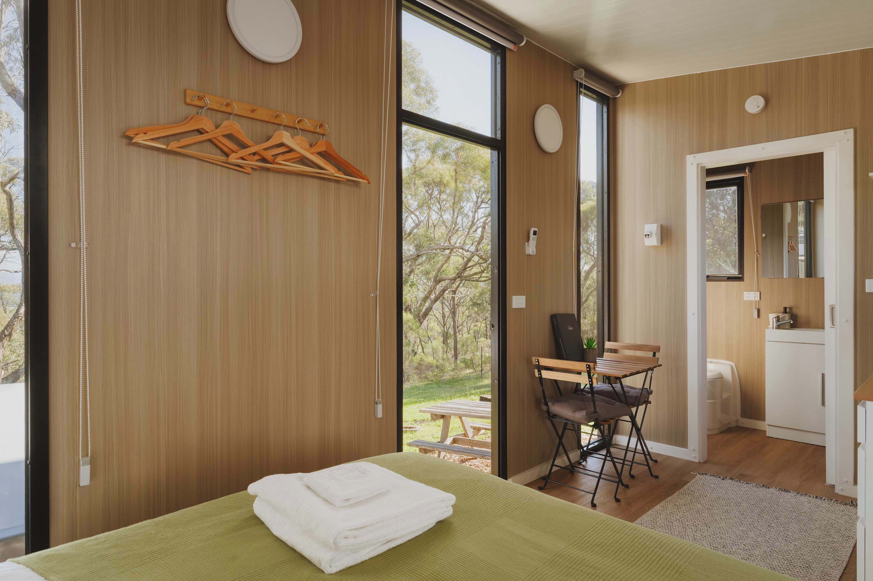 Een moderne slaapkamer met een groot bed, een houten kapstok, een bureau met stoel, en een badkamer met spiegel.