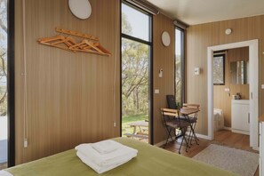 Ein modernes Schlafzimmer mit einem großen Bett, einem Holz-Kleiderständer, einem Schreibtisch mit Stuhl und einem Badezimmer mit Spiegel.