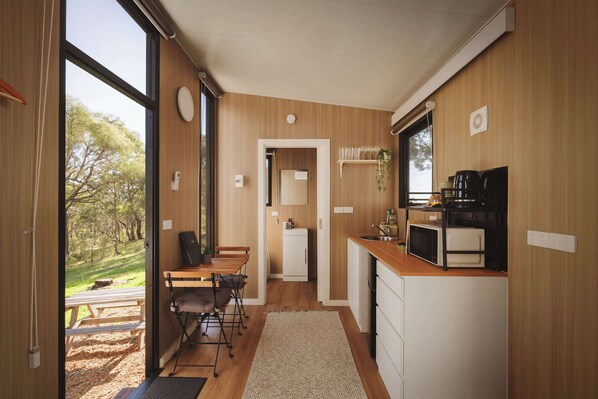 A compact kitchen with wooden cabinetry, a dining area with a table and chairs, and a view of the outdoors through large windows.