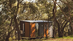A small, single-story cabin with a metal roof, surrounded by trees. - Tallarook Hilltop Tiny House 4 by Tiny Away (Tallarook)