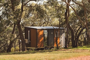 A small, single-story cabin with a metal roof, surrounded by trees.