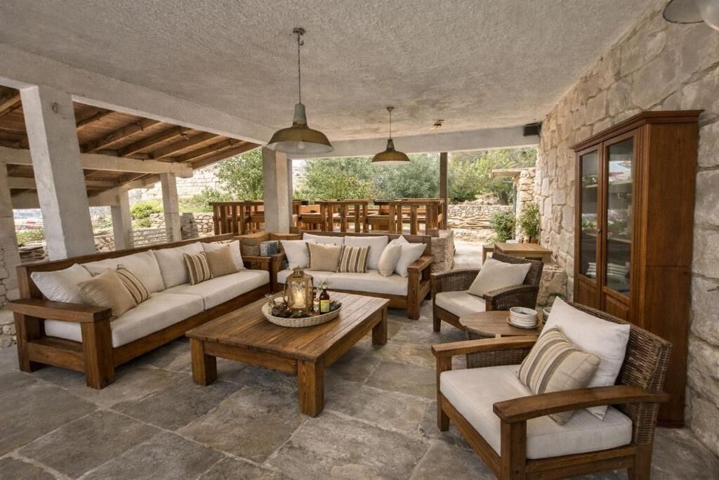 Un espacio al aire libre techado con mobiliario de madera, paredes de piedra y lámparas colgantes.