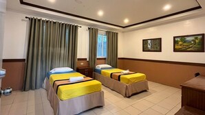 Camera d'albergo con due letti singoli, una scrivania, una sedia, una finestra con tende e una parete decorata con due quadri.