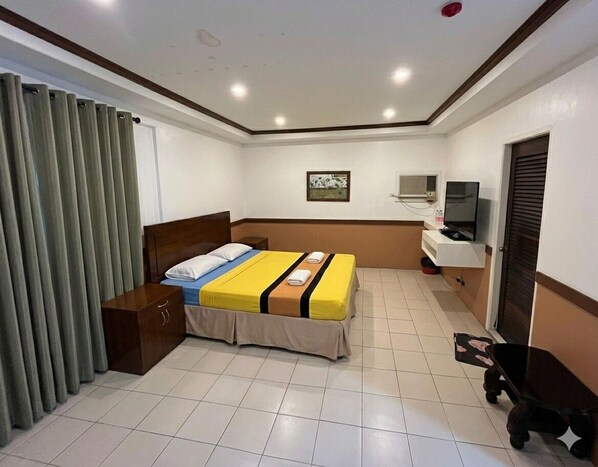 A hotel room with a bed, a TV, a wardrobe, and a desk. - Topaz House By Gems Hotel (Antipolo)
