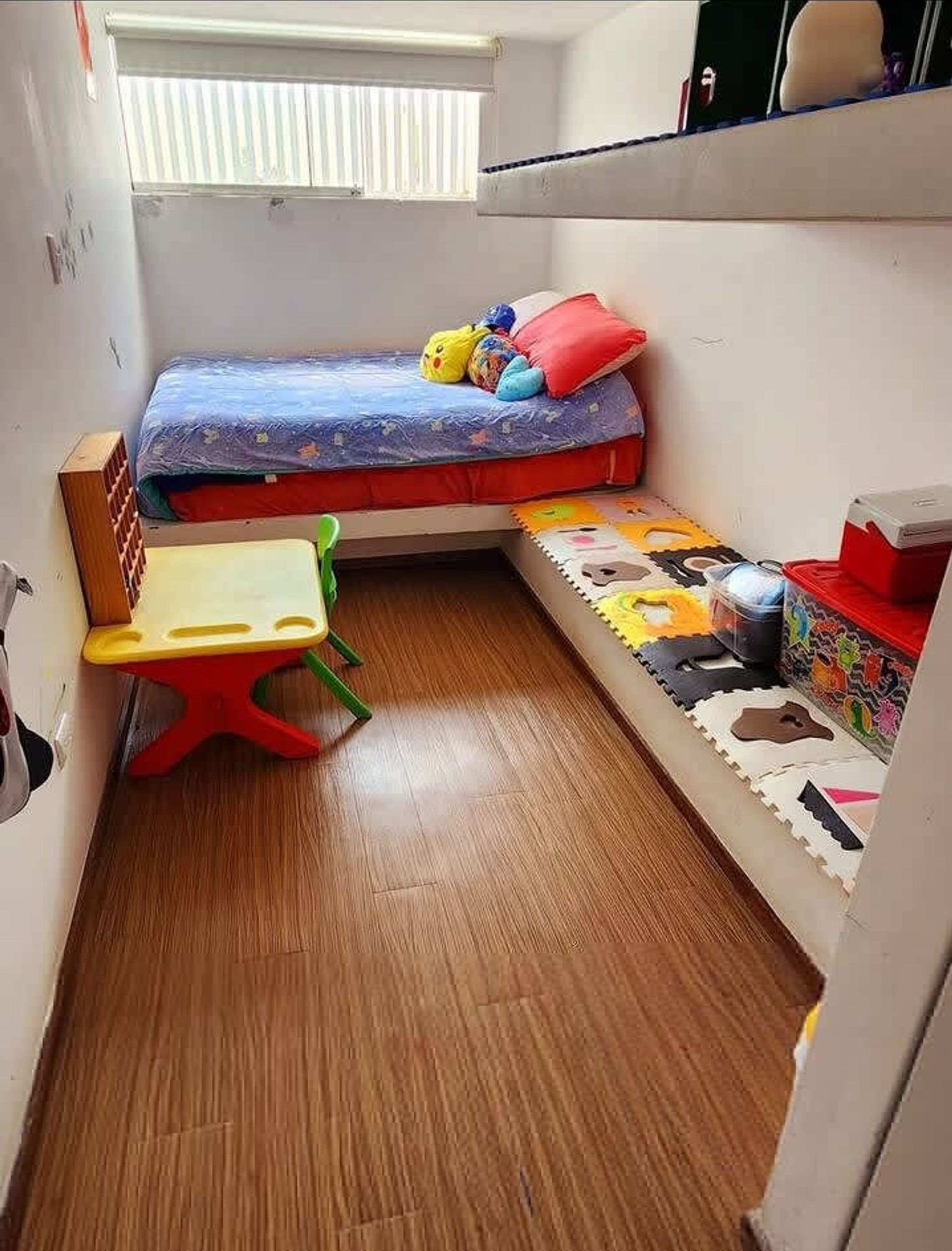 A small, compact room with a bunk bed, a small table, and a storage unit.