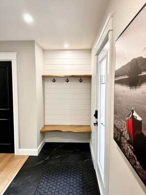 A hallway with a wooden bench, white walls, a black tiled floor, and a door with a coat hanging.