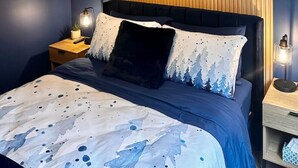 Et soveværelse med en seng, et natbord, et billede på væggen og en lampe i loftet.