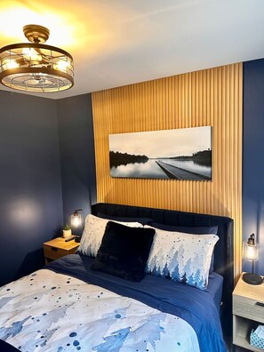 A bedroom with a bed, a nightstand, a wall-mounted picture, and a ceiling light fixture.
