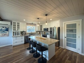 A modern kitchen with a central island, bar stools, and a view of the ocean through a window.