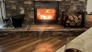 A fireplace with logs, a glass of red wine, and a stone wall.